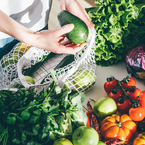 A display of fresh fruit and vegetables being unpacked from a reusable grocery bag. 